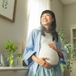 The reality of pregnancy after 35 (hint: it’s not all risk) Pregnant woman cradles baby bump while smiling.